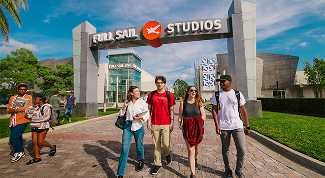 Four students walk under the Full Sail Studios archway with Full Sail Live behind them.