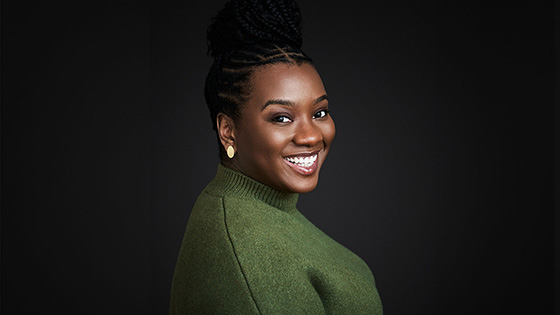 CeCe Taylor smiles at the camera. Her hair is up in a braided bun and she’s wearing a green sweater and gold earrings.