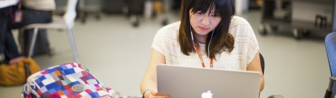 A student stares intently at her MacBook, while a colorful backpack rests on the table.