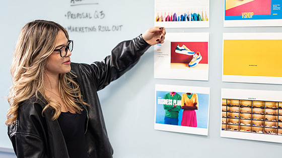 A woman is in front of a whiteboard with colorful designs, in a modern workspace.